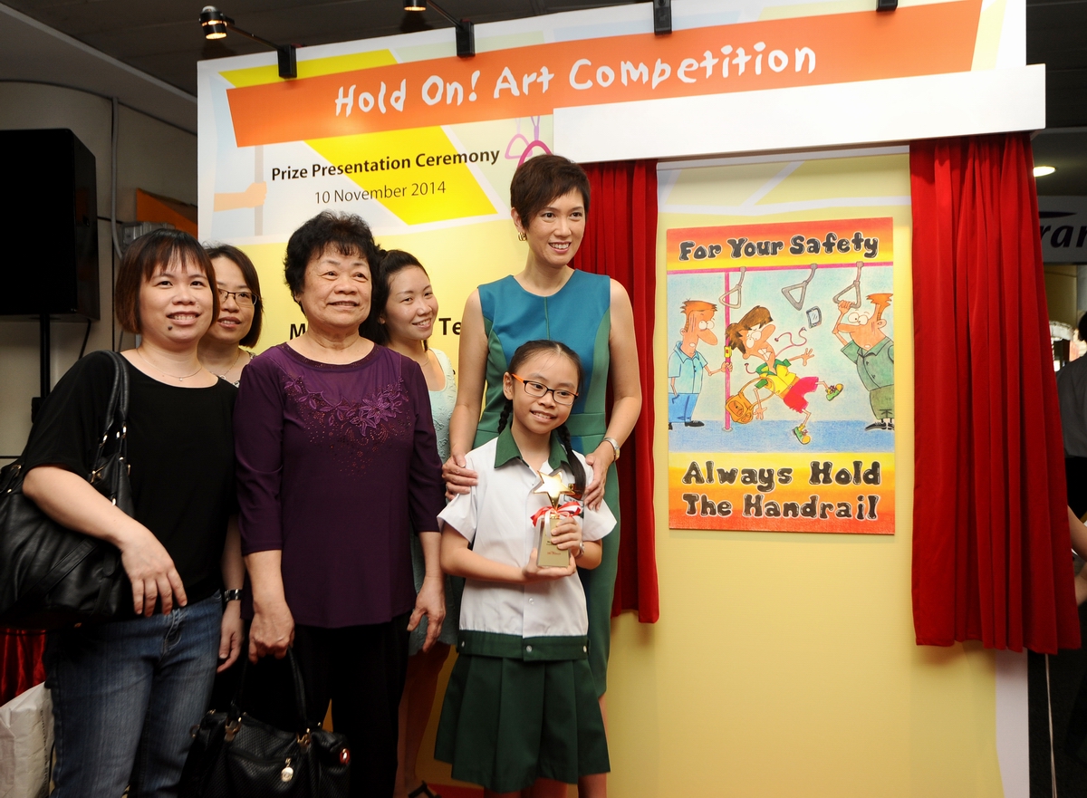 Nine-year-old Ms Tan Hui Xin posing with her family members, teachers and the Senior Minister of State for Finance and Transport with her winning entry in the background.